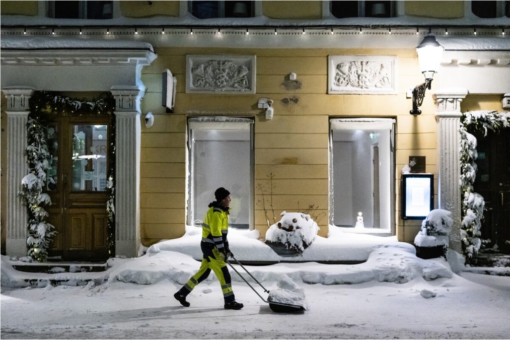 Mies tekemässä lumitöitä keskustassa yöllä kolalla.