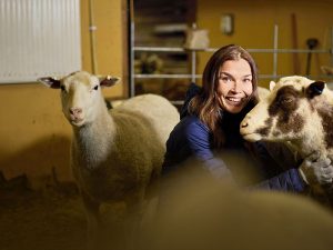 Katri Virtanen lampaiden keskellä Haltialan kotieläintilan lampolassa.