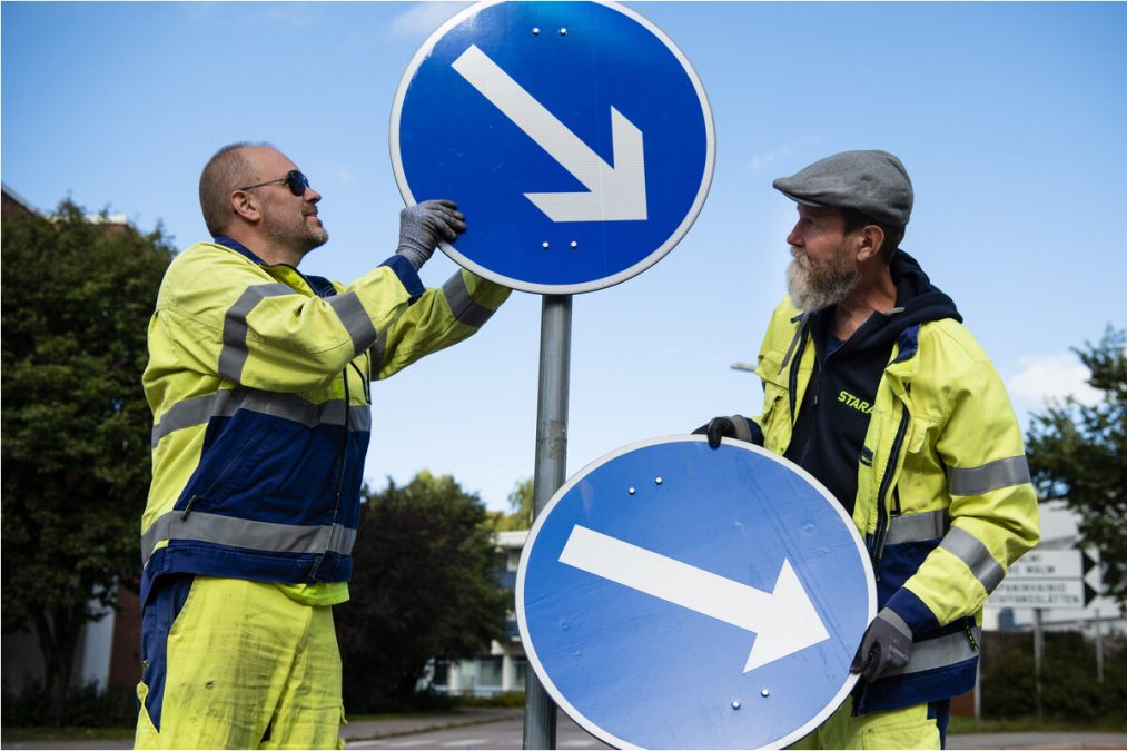 Kaksi staralaista vaihtaa liikennemerkkejä uusiin.